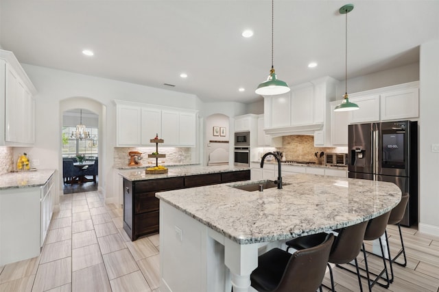 2602 Cypress Dr, Rockwall, TX 75087 - kitchen featuring backsplash, appliances with stainless steel finishes, arched walkways, a sink, and an island with sink
