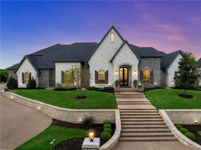 french country home with a front lawn, a shingled roof, stone siding, and french doors