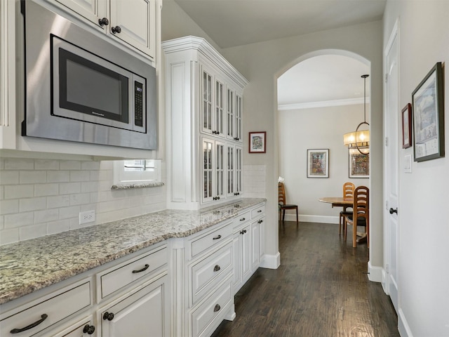 kitchen featuring tasteful backsplash, arched walkways, white cabinetry, stainless steel microwave, and dark wood-style flooring