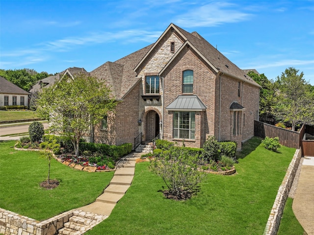 tudor home featuring brick siding, stone siding, fence, a front lawn, and a shingled roof