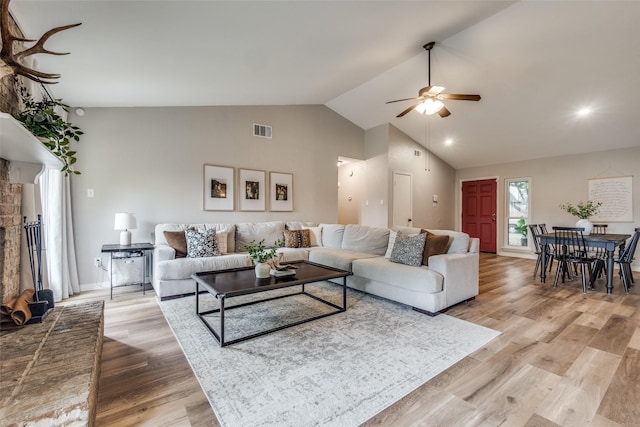 living room featuring high vaulted ceiling, a brick fireplace, light wood-style flooring, visible vents, and ceiling fan
