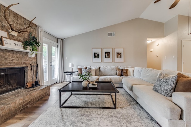 living area with a ceiling fan, wood finished floors, a brick fireplace, lofted ceiling, and visible vents