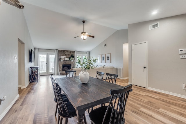dining area with visible vents, baseboards, ceiling fan, a stone fireplace, and light wood-style floors