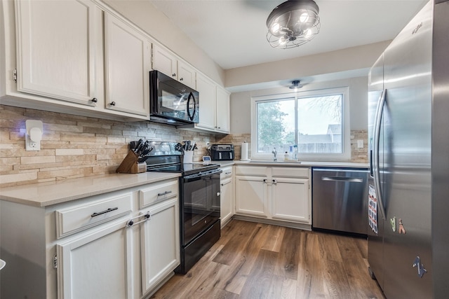 kitchen featuring light countertops, a sink, tasteful backsplash, wood finished floors, and black appliances