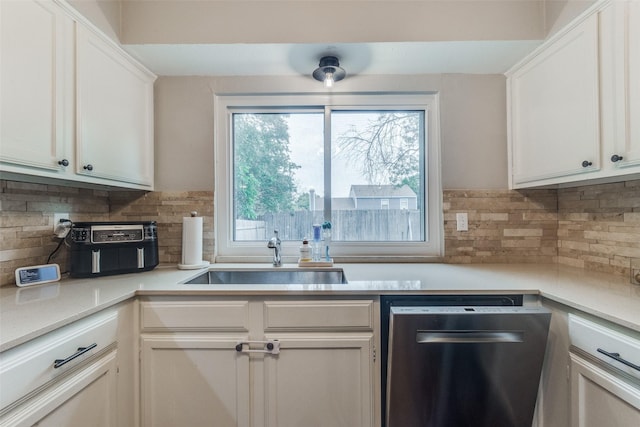 kitchen featuring light countertops, stainless steel dishwasher, backsplash, a sink, and white cabinets