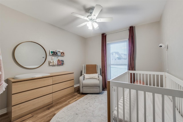 bedroom featuring light wood-style flooring, baseboards, a nursery area, and ceiling fan