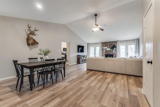 dining room featuring high vaulted ceiling, a stone fireplace, baseboards, light wood-style floors, and ceiling fan