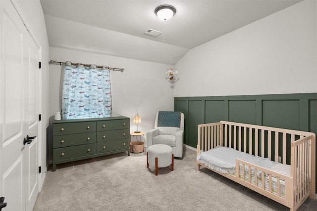 carpeted bedroom with a closet, a crib, lofted ceiling, a decorative wall, and visible vents