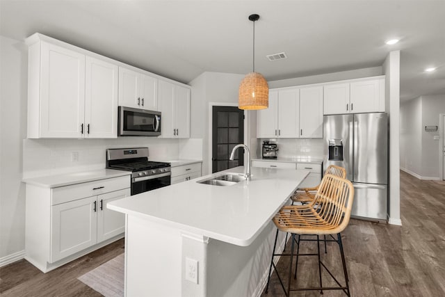 kitchen featuring a sink, stainless steel appliances, a kitchen island with sink, visible vents, and dark wood-type flooring