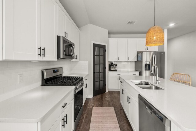 kitchen with a sink, appliances with stainless steel finishes, hanging light fixtures, visible vents, and dark wood-style flooring