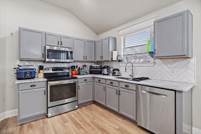3968 Hunter Peak Rd, Fort Worth, TX 76262 - kitchen with stainless steel appliances, gray cabinets, vaulted ceiling, light wood-style flooring, and tasteful backsplash