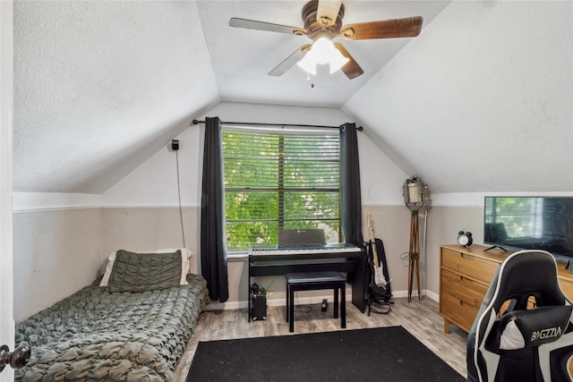 bedroom with baseboards, a ceiling fan, a textured ceiling, wood finished floors, and lofted ceiling