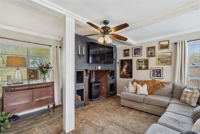 living room with a ceiling fan, wood finished floors, a wood stove, and ornamental molding