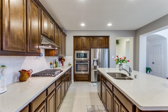 kitchen featuring under cabinet range hood, a sink, a kitchen island with sink, tasteful backsplash, and appliances with stainless steel finishes