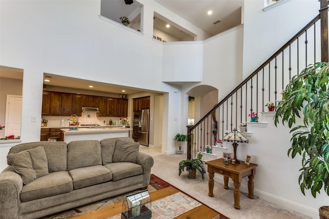 living area featuring recessed lighting, a high ceiling, arched walkways, baseboards, and stairs