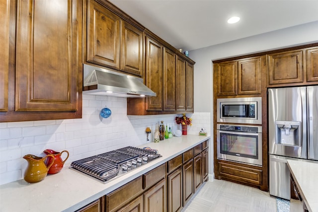 kitchen featuring light countertops, decorative backsplash, appliances with stainless steel finishes, and under cabinet range hood