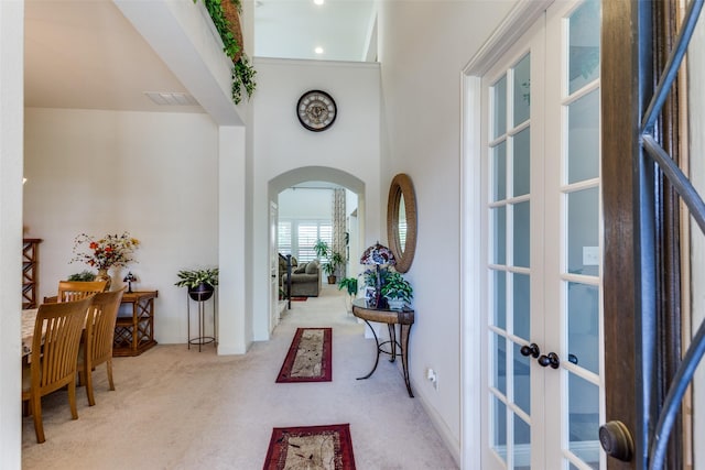 carpeted entrance foyer with arched walkways, french doors, visible vents, and baseboards