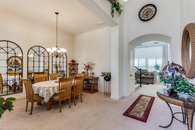 dining area featuring carpet flooring, arched walkways, visible vents, a towering ceiling, and a chandelier