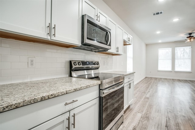 kitchen featuring light stone countertops, appliances with stainless steel finishes, visible vents, light wood-style floors, and decorative backsplash