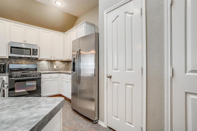 kitchen with lofted ceiling, backsplash, appliances with stainless steel finishes, and white cabinets