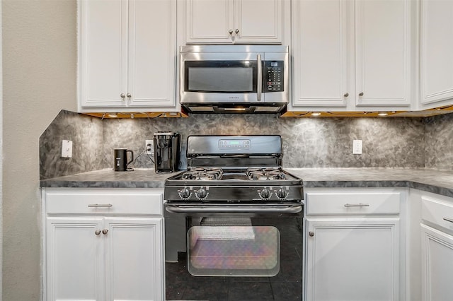 kitchen with white cabinetry, black range with gas cooktop, tasteful backsplash, stainless steel microwave, and dark countertops