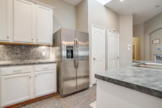 kitchen featuring a sink, backsplash, stainless steel refrigerator with ice dispenser, dark countertops, and white cabinets