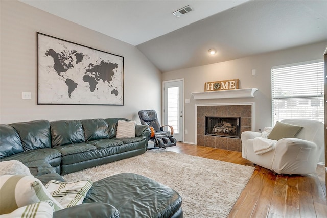 living room with a tiled fireplace, visible vents, vaulted ceiling, and wood finished floors