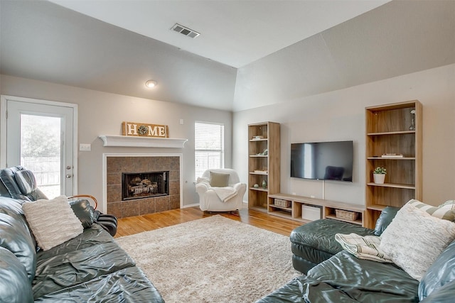 living area featuring visible vents, wood finished floors, a tile fireplace, and vaulted ceiling