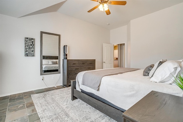 bedroom with a ceiling fan, stone finish flooring, baseboards, and vaulted ceiling