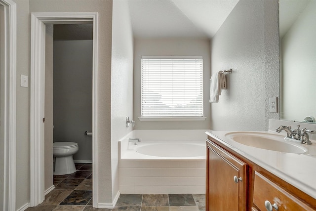 bathroom with a textured wall, toilet, vanity, and a garden tub