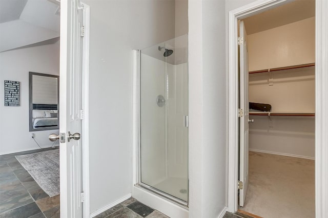bathroom with a spacious closet, a stall shower, baseboards, and vaulted ceiling