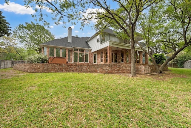 back of property featuring a storage unit, a chimney, fence, brick siding, and a yard