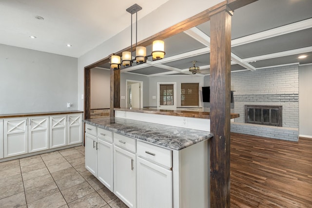 2306 Ravenwood Dr, Grand Prairie, TX 75050 - kitchen with a ceiling fan, white cabinets, a fireplace, dark stone counters, and decorative light fixtures