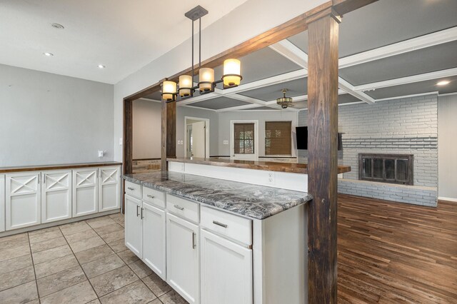 2306 Ravenwood Dr, Grand Prairie, TX 75050 - kitchen featuring a ceiling fan, white cabinetry, a brick fireplace, dark stone countertops, and hanging light fixtures
