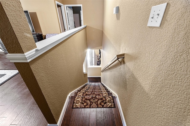 stairs featuring baseboards, a textured wall, and wood finished floors