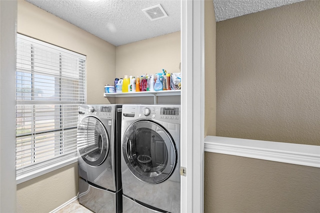 clothes washing area with washing machine and clothes dryer, visible vents, a textured ceiling, and laundry area