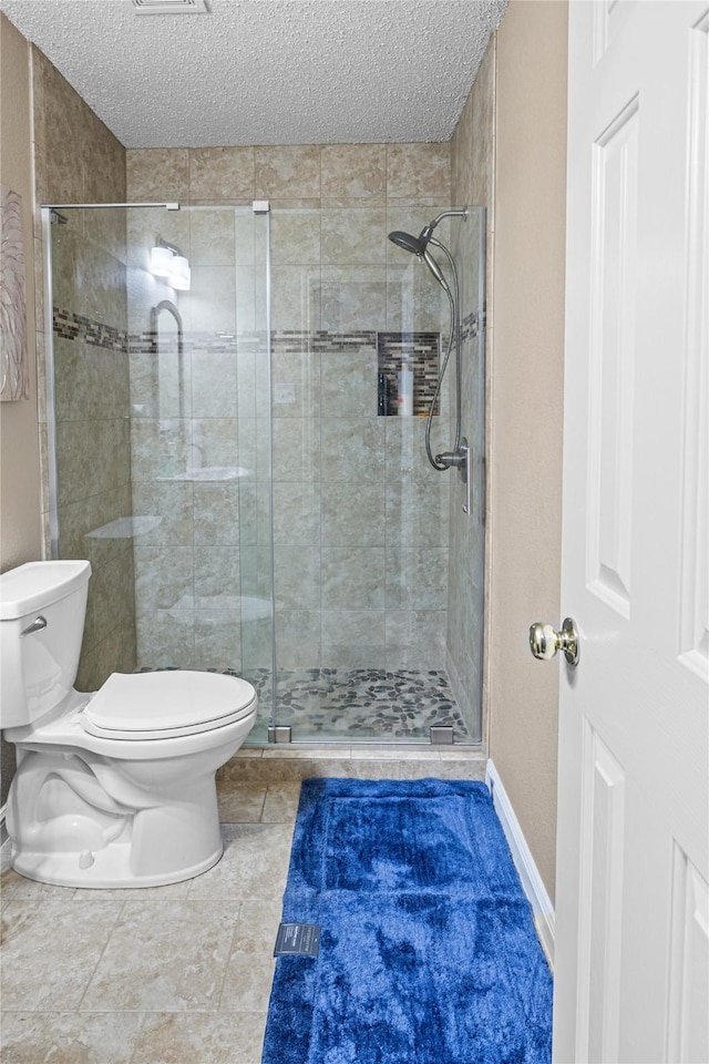 bathroom with baseboards, a textured ceiling, toilet, and a stall shower