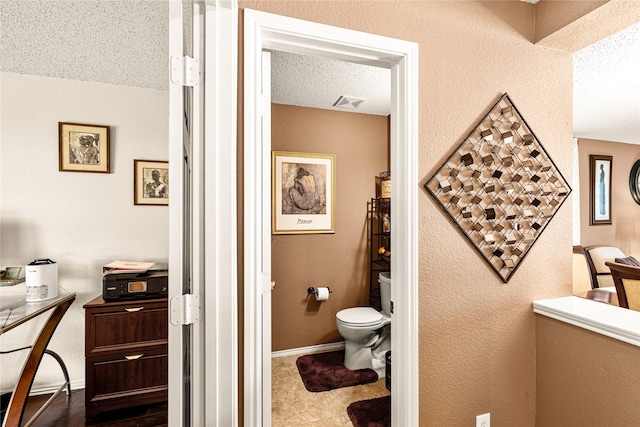 bathroom featuring a textured wall, baseboards, visible vents, and toilet