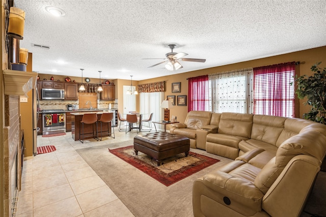 living area featuring a ceiling fan, a textured ceiling, light tile patterned floors, light colored carpet, and visible vents