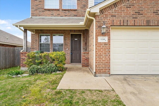 doorway to property with concrete driveway, brick siding, an attached garage, and fence
