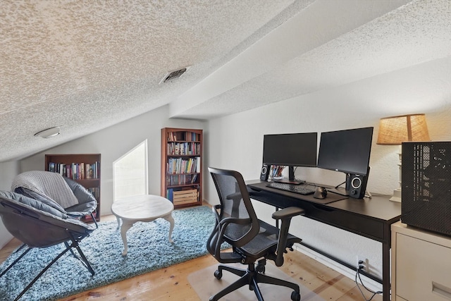 home office with visible vents, lofted ceiling, wood finished floors, and a textured ceiling