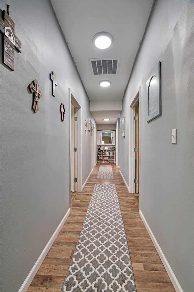 hall with visible vents, baseboards, and wood finished floors
