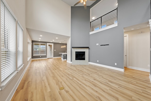 unfurnished living room with light wood-type flooring, baseboards, a fireplace, stairs, and ceiling fan