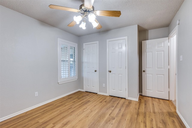 unfurnished bedroom with two closets, baseboards, a textured ceiling, and light wood-style floors