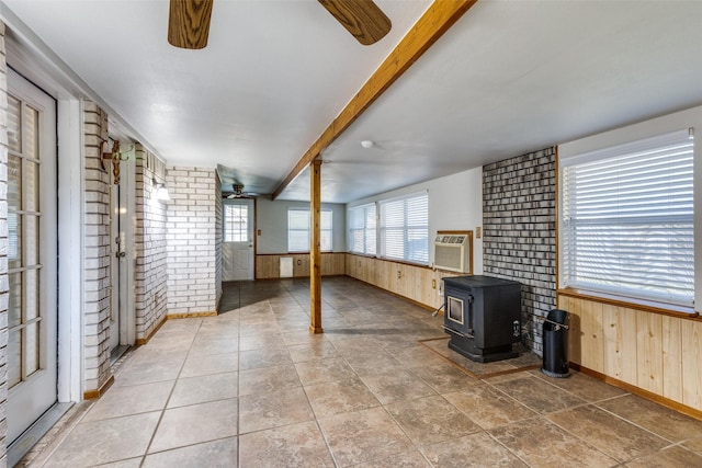 unfurnished living room featuring brick wall, wood walls, baseboards, and ceiling fan