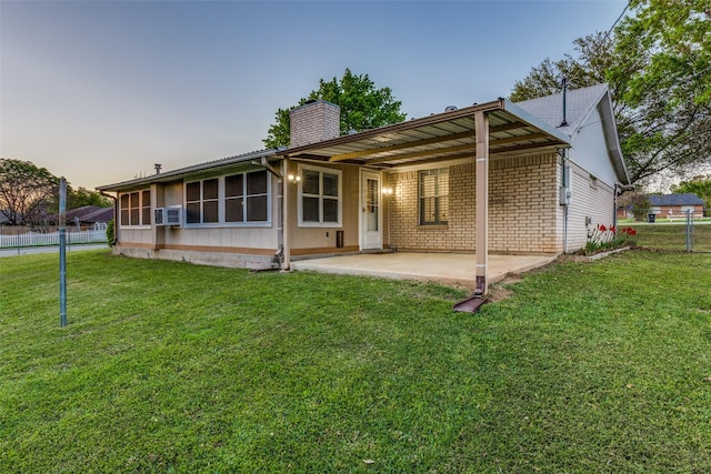 back of property with a lawn, a patio area, fence, a chimney, and an attached carport