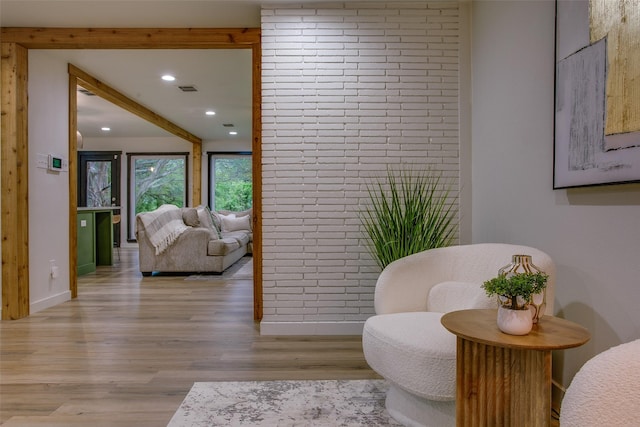 living area with beamed ceiling, light wood finished floors, baseboards, recessed lighting, and brick wall