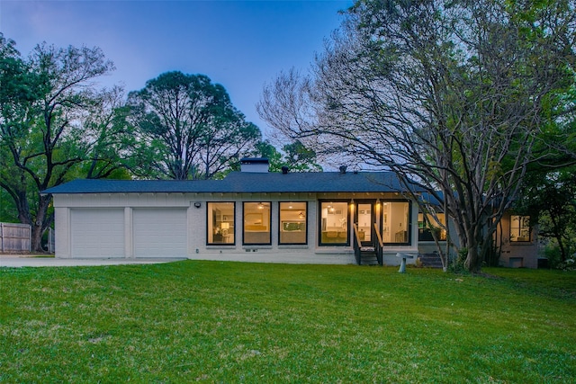 rear view of property featuring driveway, a chimney, a garage, and a yard