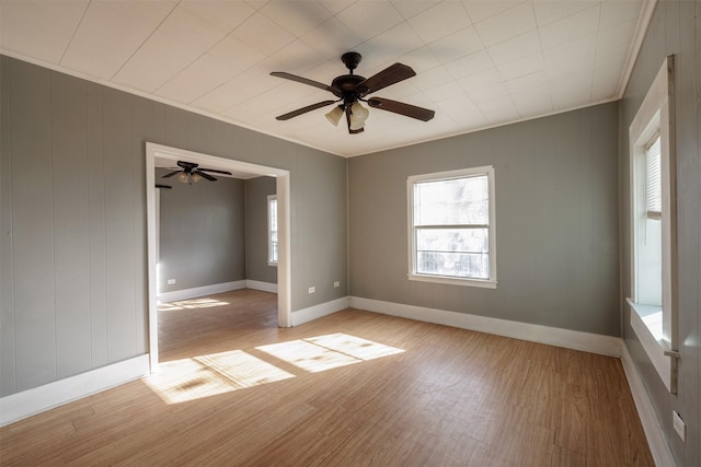 empty room featuring baseboards, a ceiling fan, light wood-style flooring, and crown molding