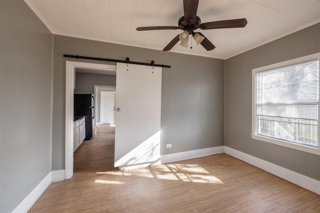 unfurnished room featuring a barn door, light wood-style flooring, ornamental molding, and a ceiling fan